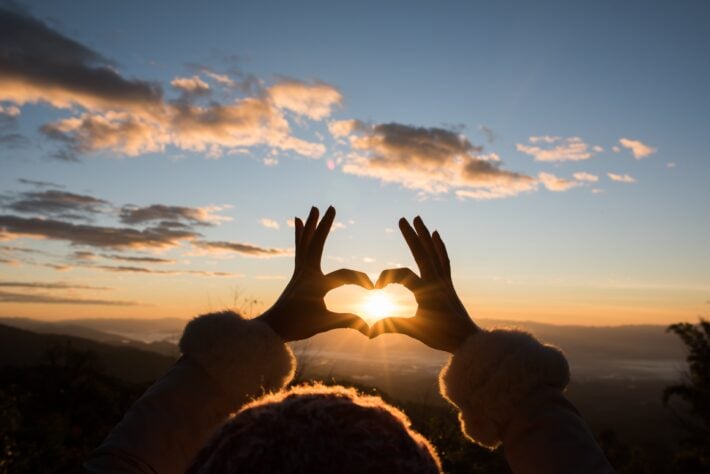 Hands in the shape of a heart over the sun